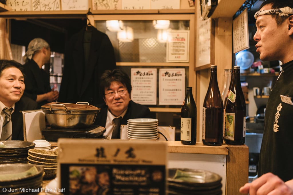 KAGOSHIMA, JAPAN - February 4, 2016: Customers exchange banters with the owner and enjoy Japanese food and drinks at an izakaya in Kagomma Furusato Yataimura. The place is a mock village of food stalls and small restaurants. Its quaint alleyways with colorful lanterns provide a glimpse into authentic Japanese dining experience.