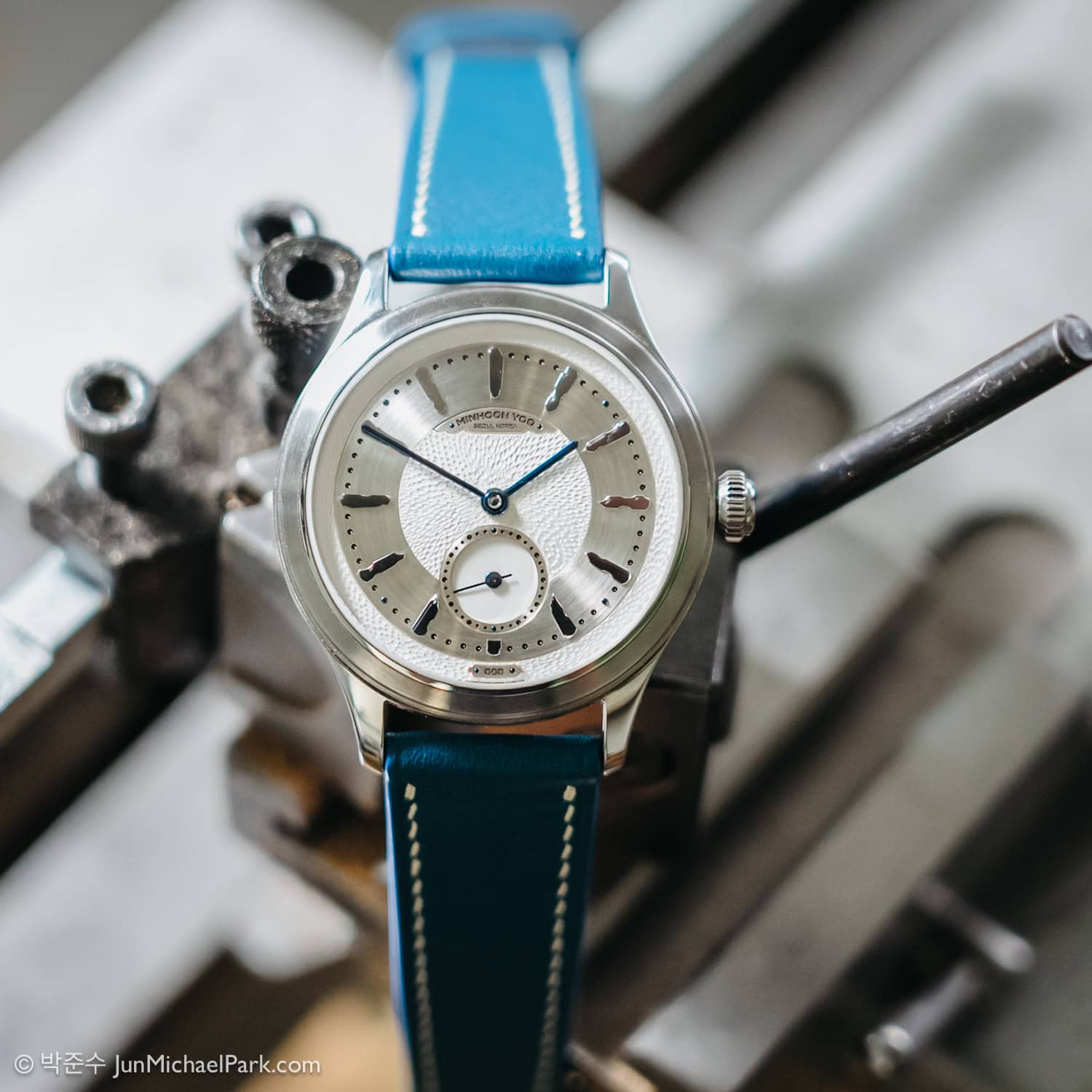 A photo of South Korean watchmaker Minhoon Yoo’s wristband watch, The Carved Piece, by photographer Jun Michael Park. The wristband is blue with two lines of white stitching close to the outlines.