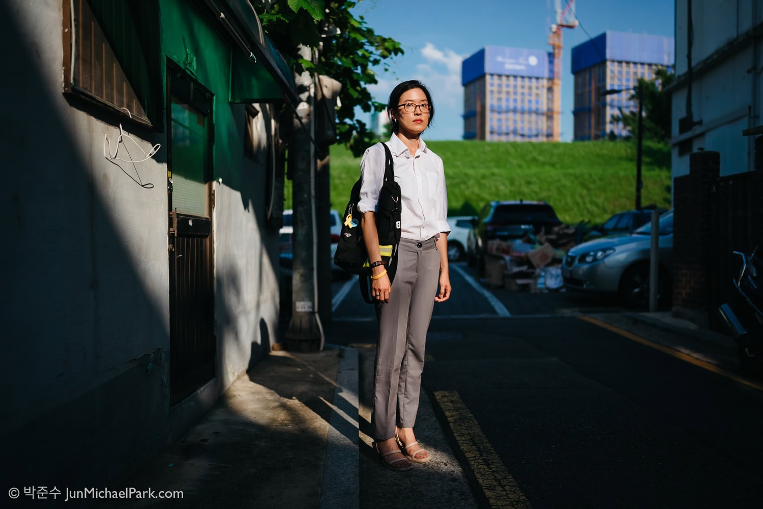 South Korean novelist Bora Chung looks at the camera at Seoul photographer Jun Michael Park's direction for a portrait. She stands in front of a shoddy house. Behind her, new apartment blocks are being built, showing a stark disparity between the rich and poor.
