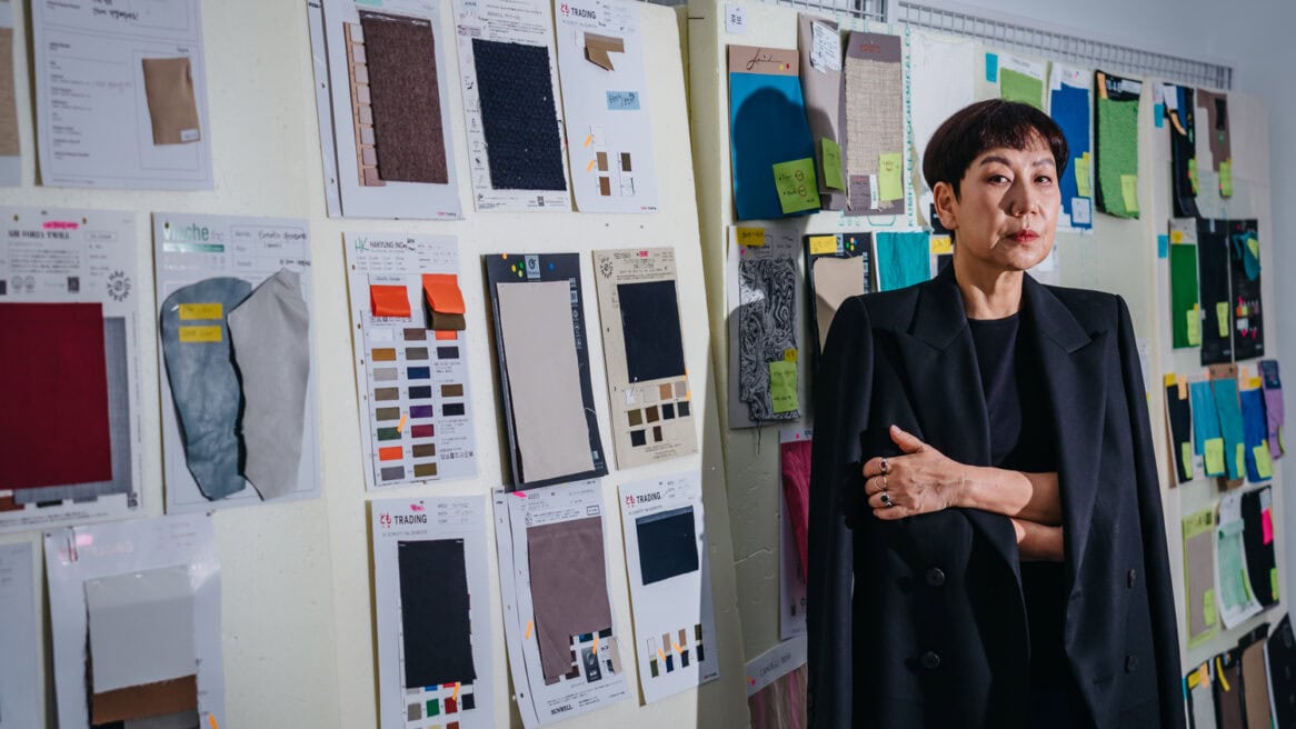 South Korean menswear designer Woo Young-mi is directed to look at the camera by photographer Jun Michael Park in a portrait setting at her studio in Seoul. She is being photographed against the wall of fabric samples.